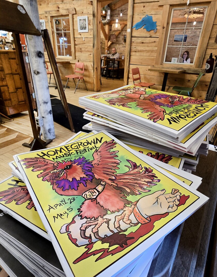 Stacks of music festival field guides show a chicken gripping a severed wrist.