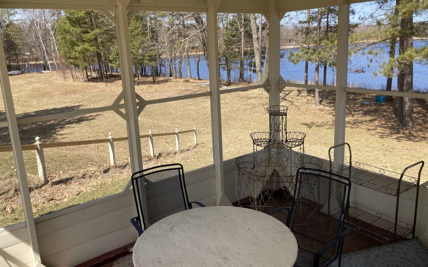 A table and chairs inside a screen house with a yard and lake in the background