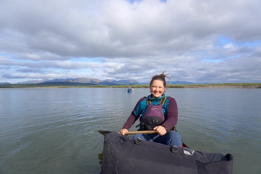 light-skinned woman wearing personal flotation device smiles as she holds paddle in canoe