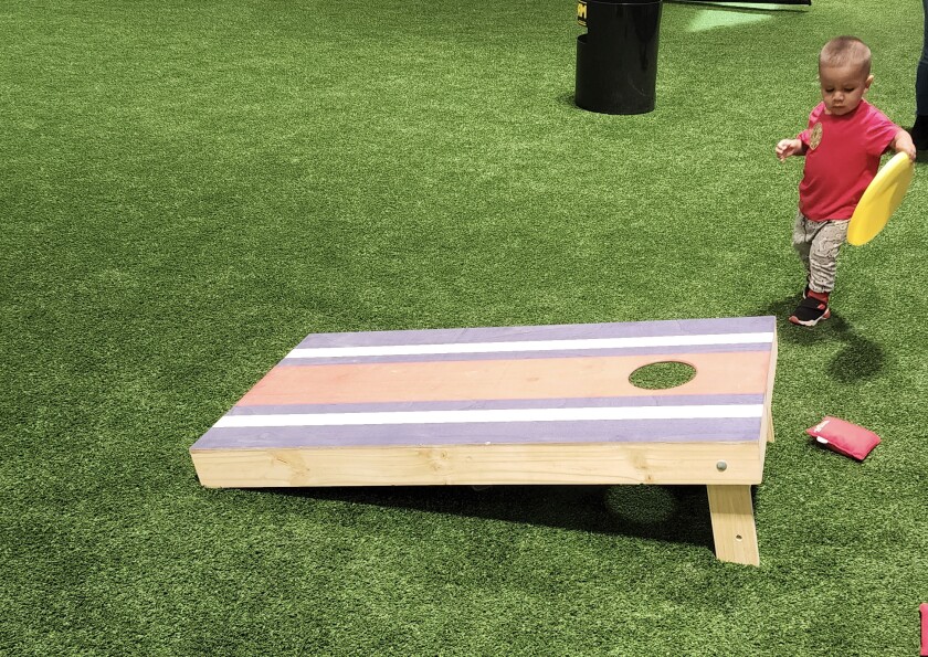 A toddler tries to join in the fun using a disc rather than a bean bag during the Night to Unite festivities Tuesday, Aug. 2, 2022 at the JBS Field House.