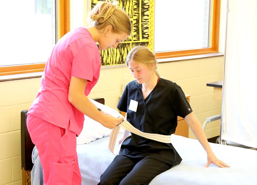 Shelby Driscoll, left, tightens a gait belt around Hattie Plasch during the CNA class at Northwestern High School