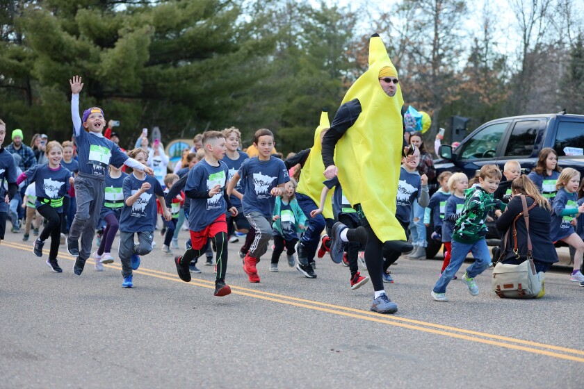Kids run down the street. A man dressed as a banana leads the pack.