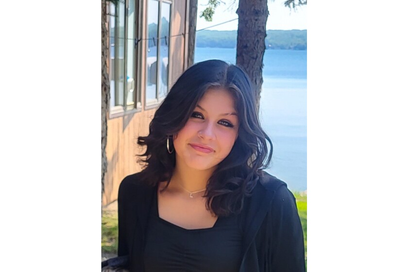 Photo of a young girl in a black top smiling in front of a lake cabin.