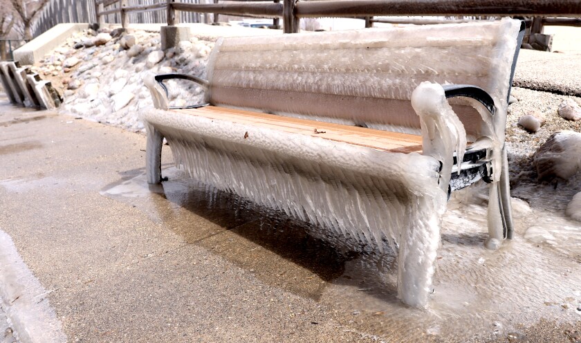 Fifty plus mile per hour wind and cold temperatures coat a bench at the outlet of Lake Okabena Thursday Afternoon in Worthington.