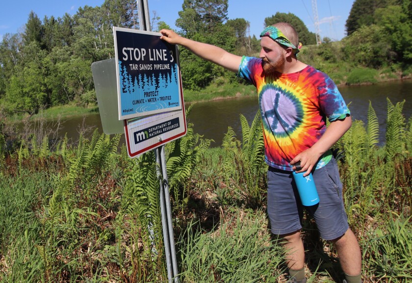 Steven Ranweiler, a student at MSUM, holds a Stop Line 3 sign over a No Trespassing sign. Enbridge Line 3 is expected to pass nearby.jpg