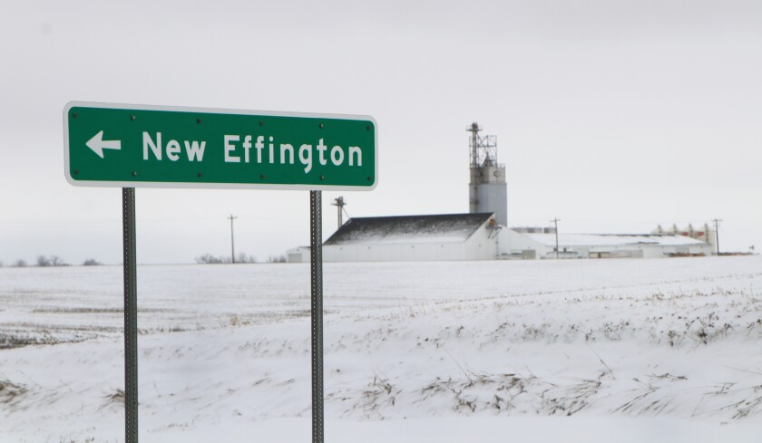 A green highway sign at New Effington, South Dakota, is flanked by a large fertilizer plant owned by Wheaton-Dumont Cooperative Elevator system, headquartered at Wheaton, Minnesota.