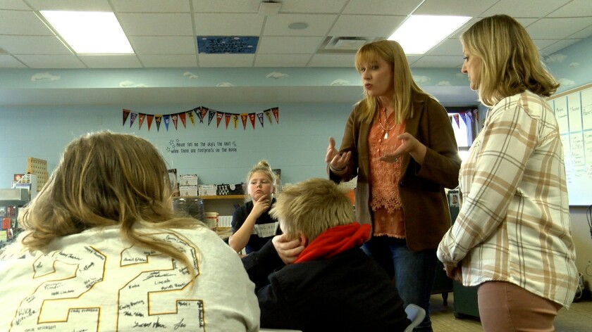 Two women at right talk to a class of students at left.