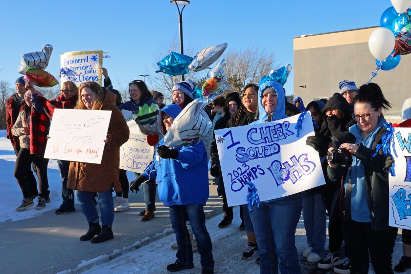 Friends and family hold signs and balloons to welcome home the cheer team.