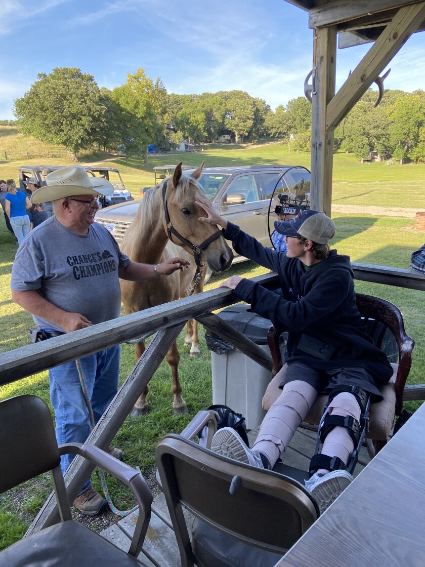 A man wearing a gray t-shirt that says Chance's Champions holds a gold-colored horse for a boy whose legs are bandaged.