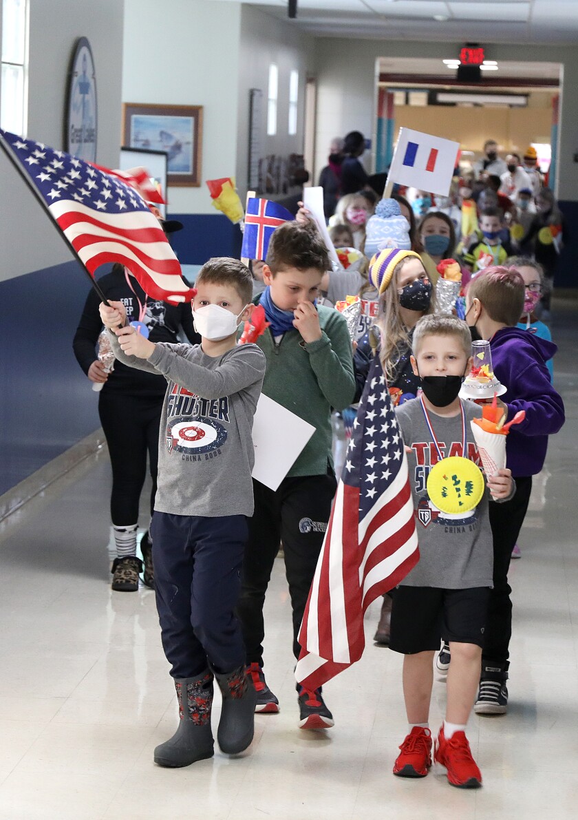 Luke, left, and Logan Shuster carry the United States flags, just like their dad, John Shuster, did earlier in the day in Beijing, China, while they lead classmates in an opening ceremony parade at Great Lakes Elementary School