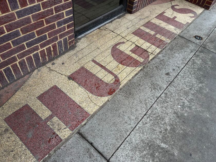 Tile on the door of an establishment, reading HUGHES on a red tile on gold.
