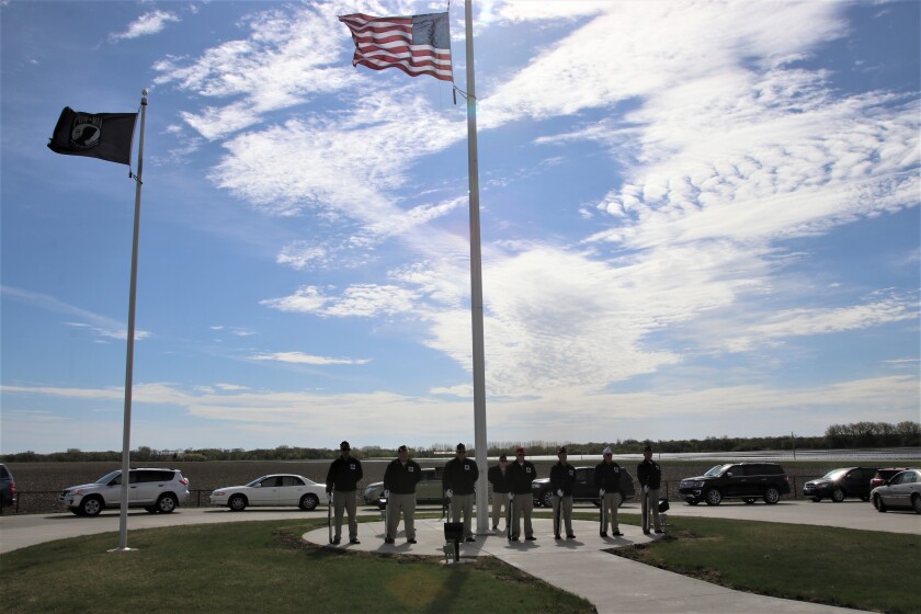 Eight veterans stand at the foot of a flagpole where the United States flag blows in the wind.