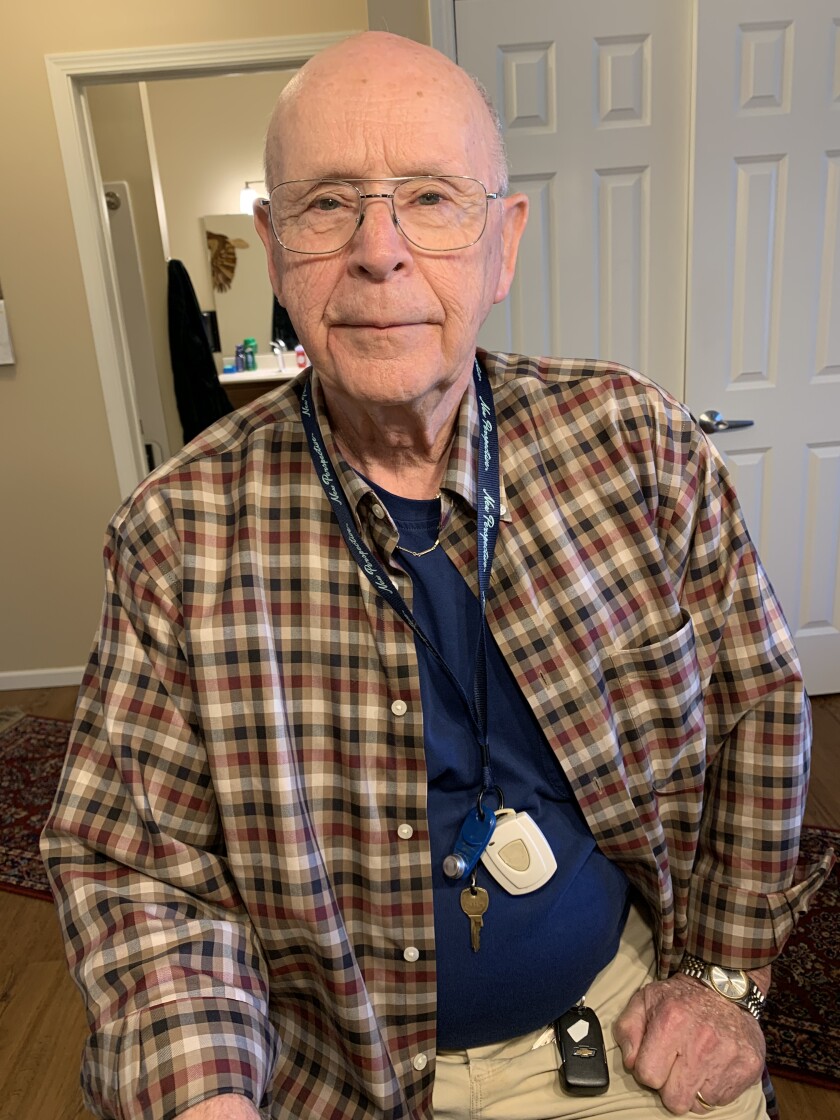 A wrinkled, bald man in a brown button-down, blue T-shirt and aviator-style glasses.