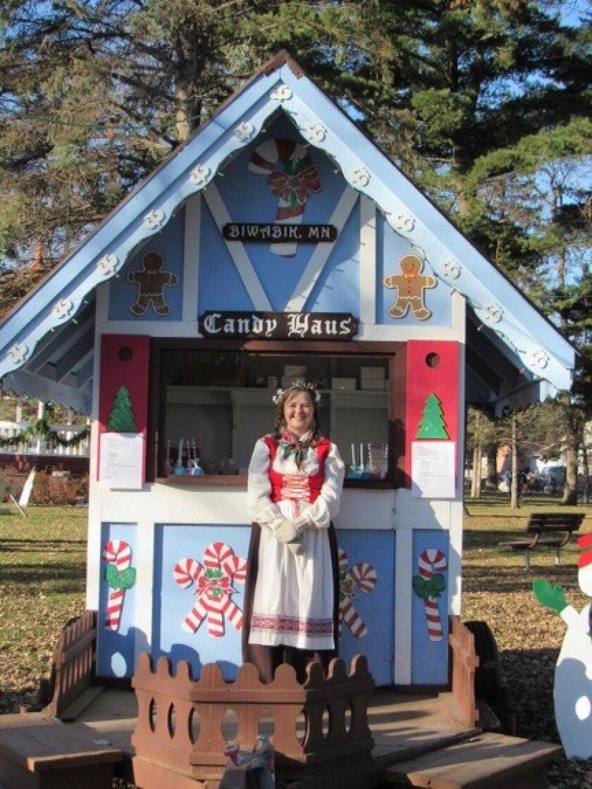 A woman dressed in a costume stands in front of a small structure labeled "Candy Haus."