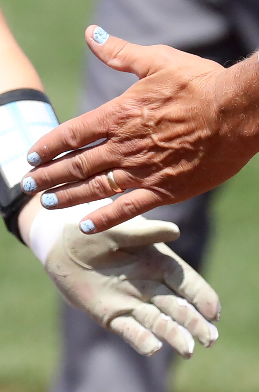 Superior first base coach John Heinen shows off his freshly painted fingernails as he gives a five to Paige Johnson