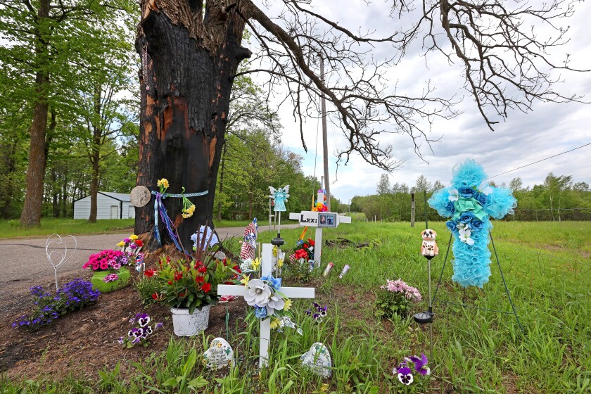 Flowers, crosses and other tokens of remembrance surround a tree.