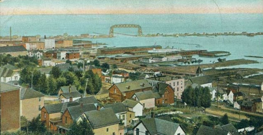 Color postcard overhead view of city with large lake and aerial bridge in background.