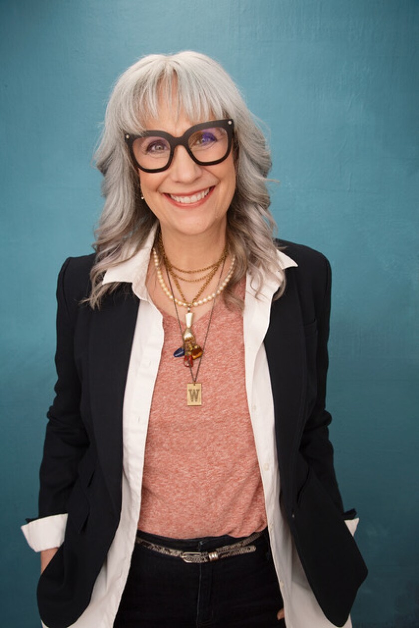 Portrait of Lizz Winstead, a slim grey-haired white woman with chunky black-rimmed glasses and a light black blazer over a red heather shirt.