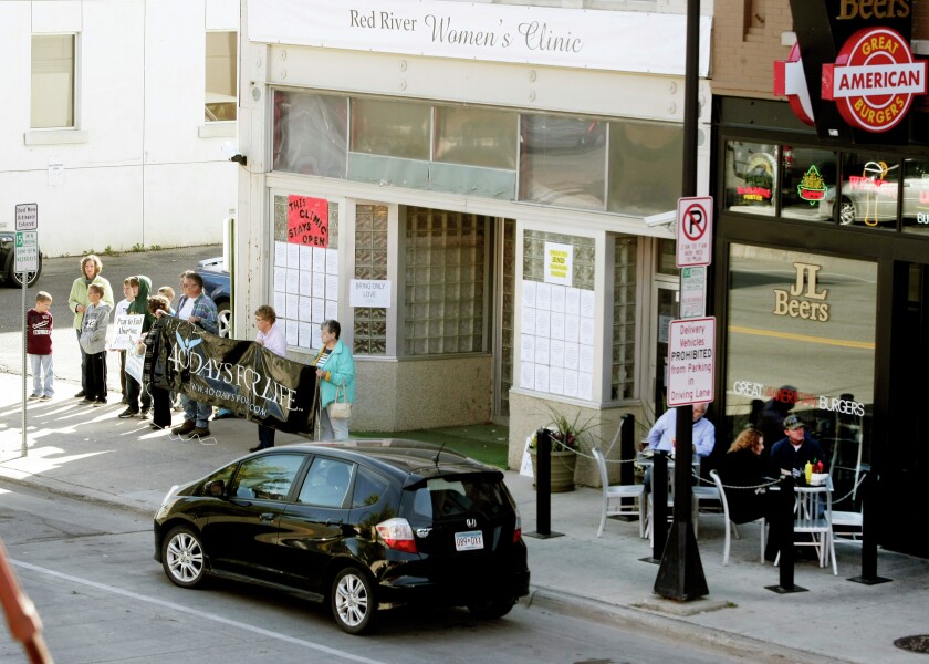 Demonstrators stand outside the Red River Women's Clinic on Oct. 9, 2013, in Fargo as lunch time customers eat outside a nearby restaurant.