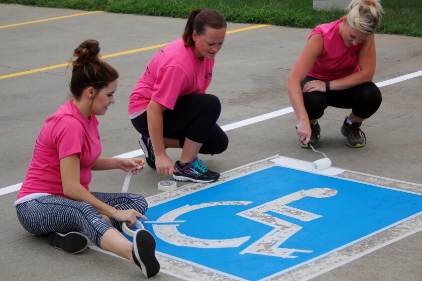 Kourtney Denne, Jen Waldera and Mary Beyer of ELO Prof. LLC repaint a parking spot outside the Mitchell Area Safehouse. (Ellen Bardash / Republic)
