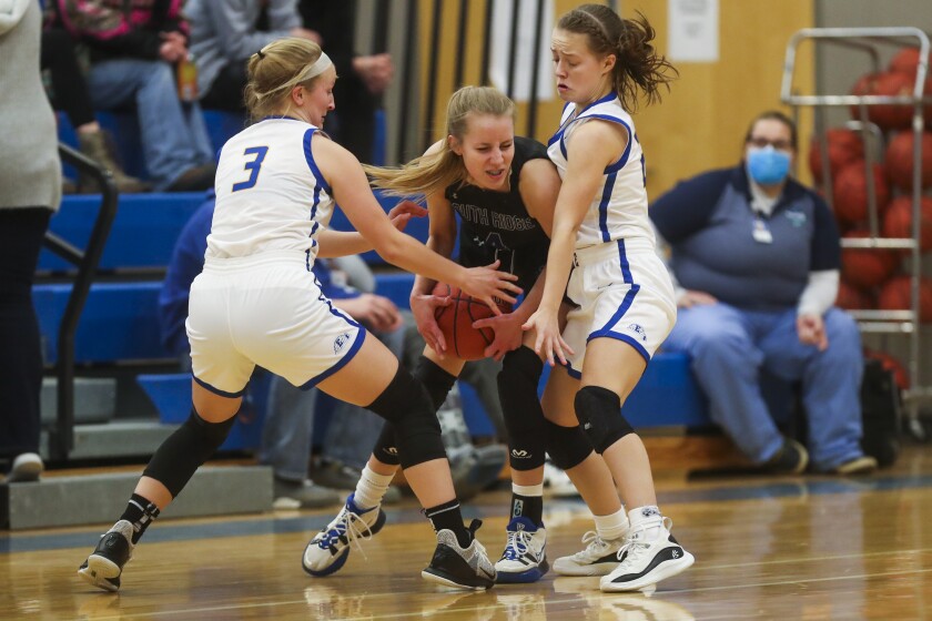 Girls basketball players in black uniforms compete against players in white uniforms at a high school gymnasium.