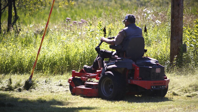 Man uses riding lawn mower to cut grass.