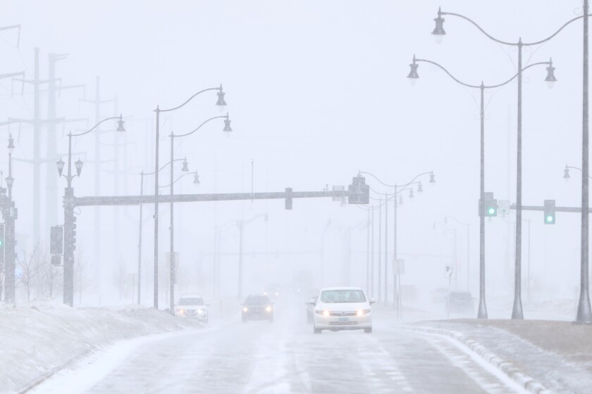 Cars drive in blowing snow which creates a foggy effect