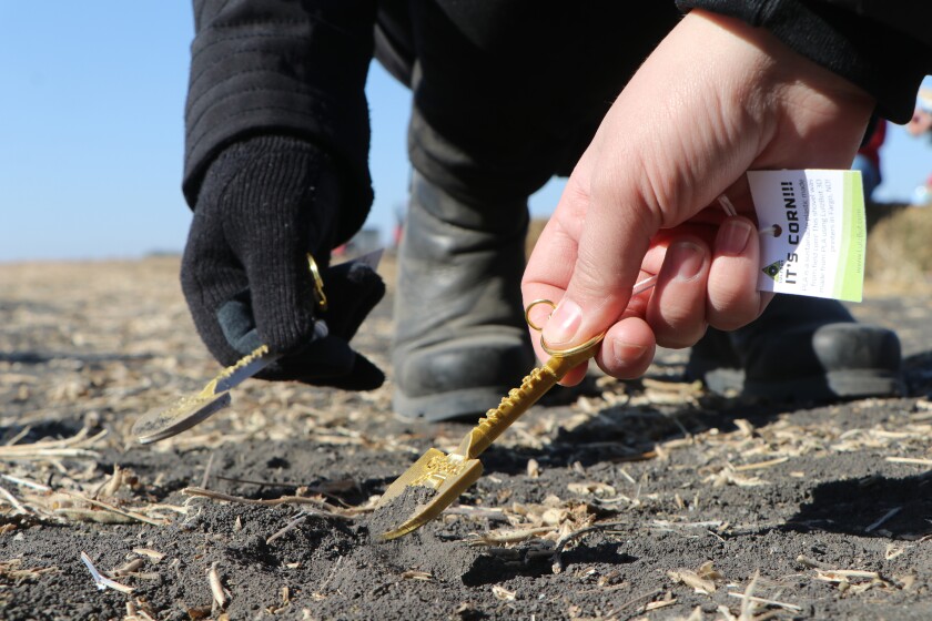 Two women use tiny, commemorative gold shovels in the soil at the Grand Farm groundbreaking.