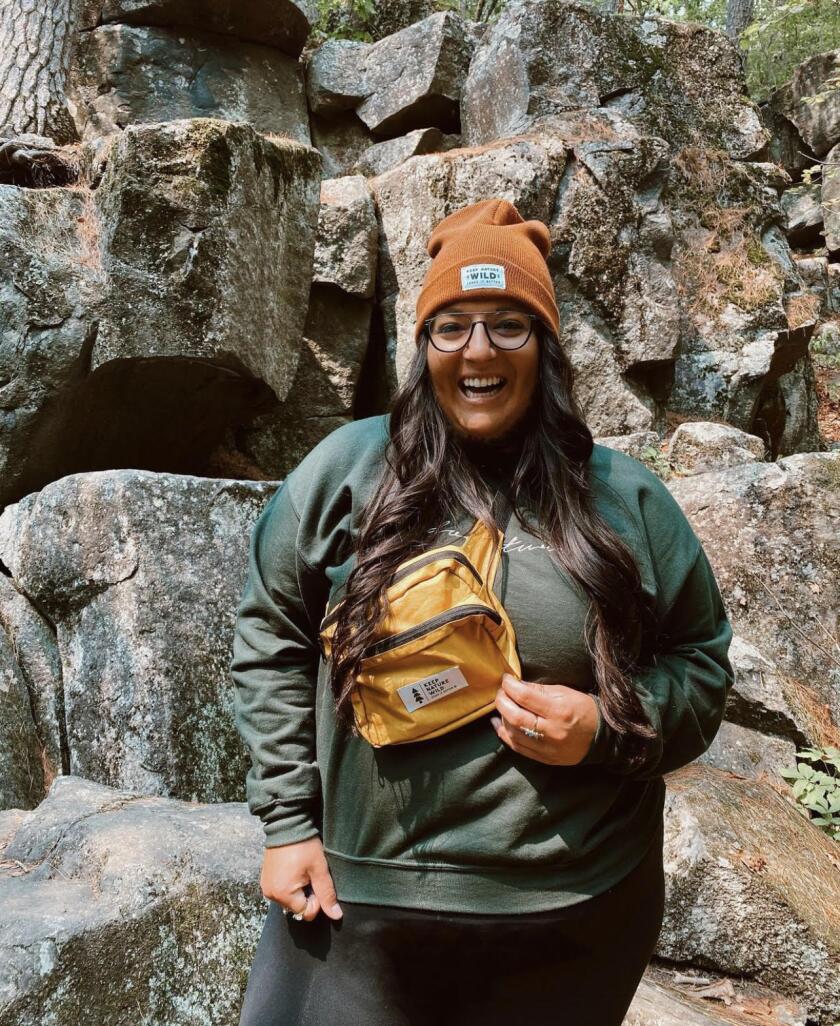 A smiling woman dressed for cool-weather hiking stands in front of a rocky backdrop.
