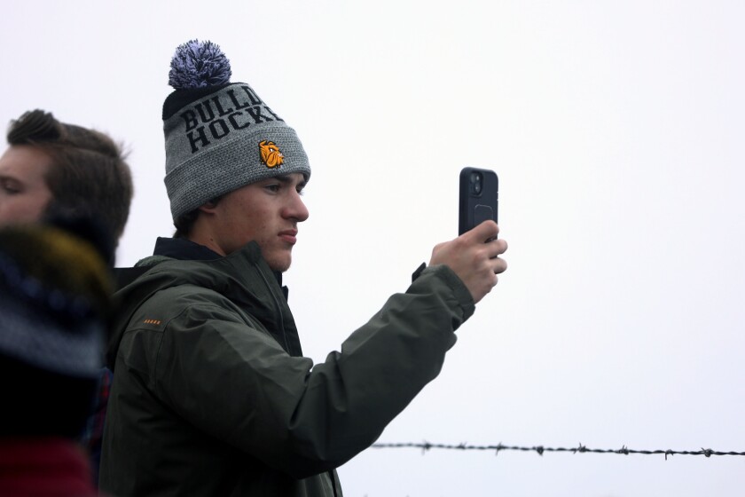 A young man using his phone to capture visuals while at an outdoor ceremony.