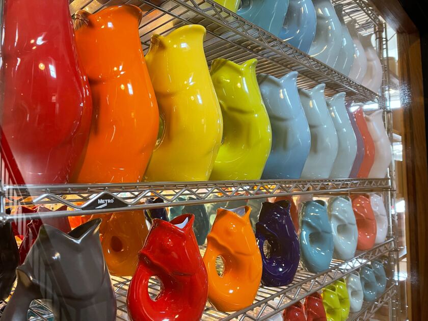 A view of store shelves displaying dozens of pitchers shaped like fish with their heads bent back to met their tails, with liquid to emerge from their mouths.