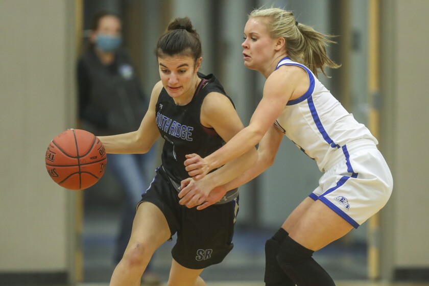 Girls basketball players in black uniforms compete against players in white uniforms at a high school gymnasium.