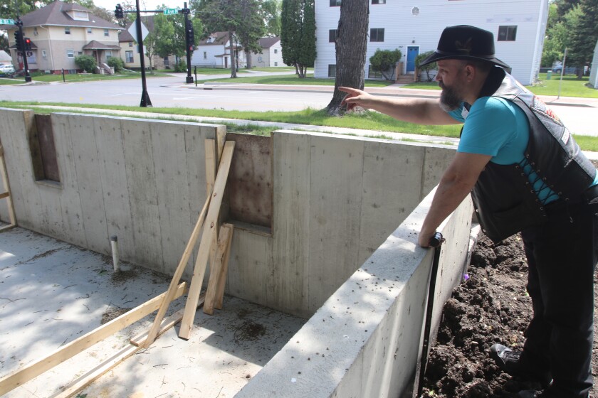 A man in a leather vest and cowboy hat leans over a foundation that does not yet have a house on it.