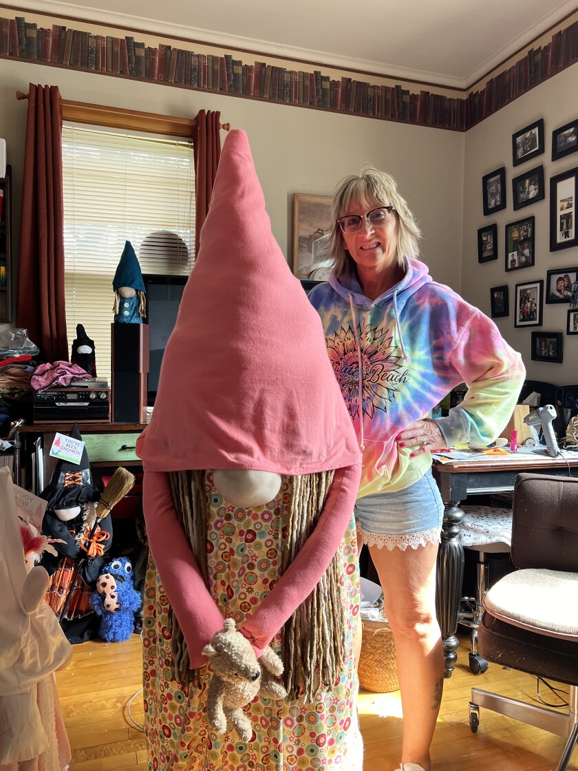 A woman in a tie-dyed sweatshirt stands beside a large gnome woman.
