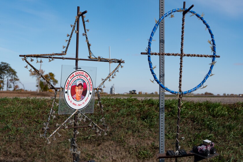 Two rustic iron markers, one bearing the photo of a young man, stand near a road