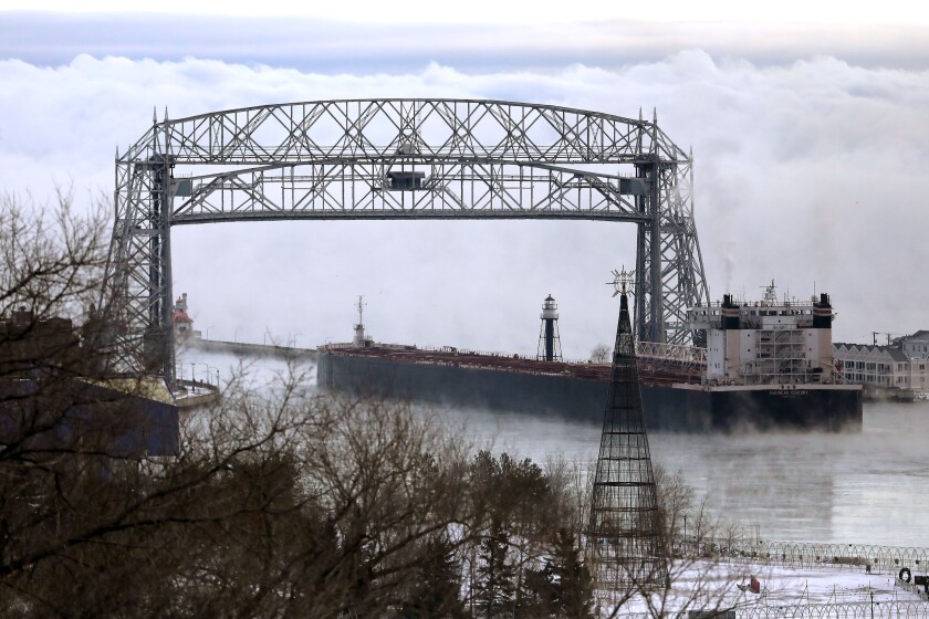 A ship traveling under a lift bridge toward sea smoke on lake superior.