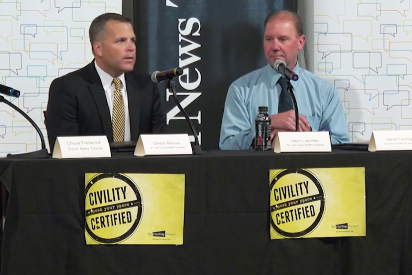 two men sit at a table with microphones