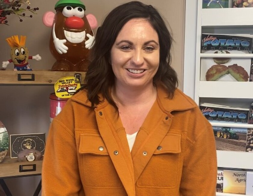 A woman with a tan jacket stands in front of potato-themed items.