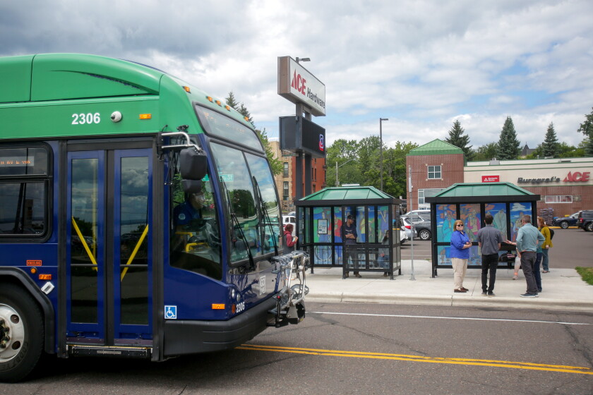 A bus traveling on a street by bus shelters and people.