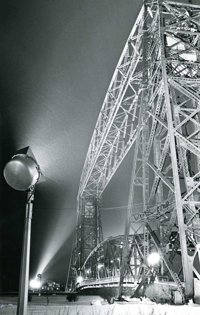 Black and white image of Aerial Lift Bridge illuminated by lights standing on poles at night.