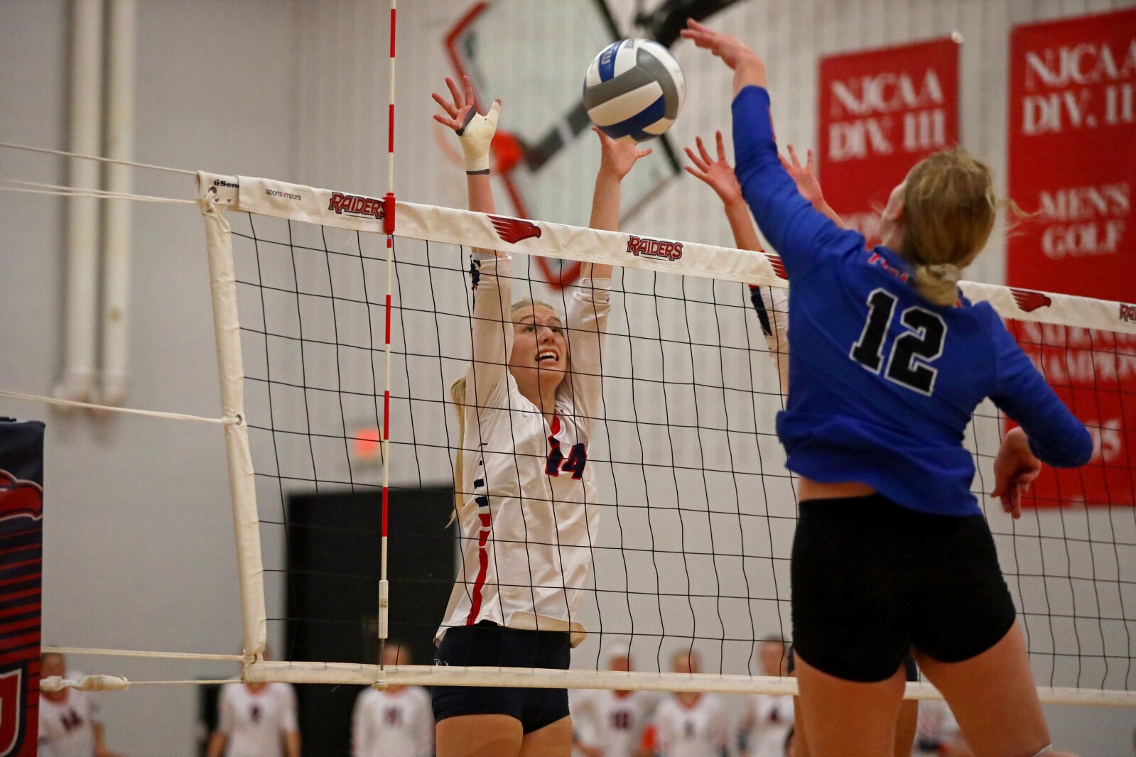 Players jumps up to stop the ball at the net.
