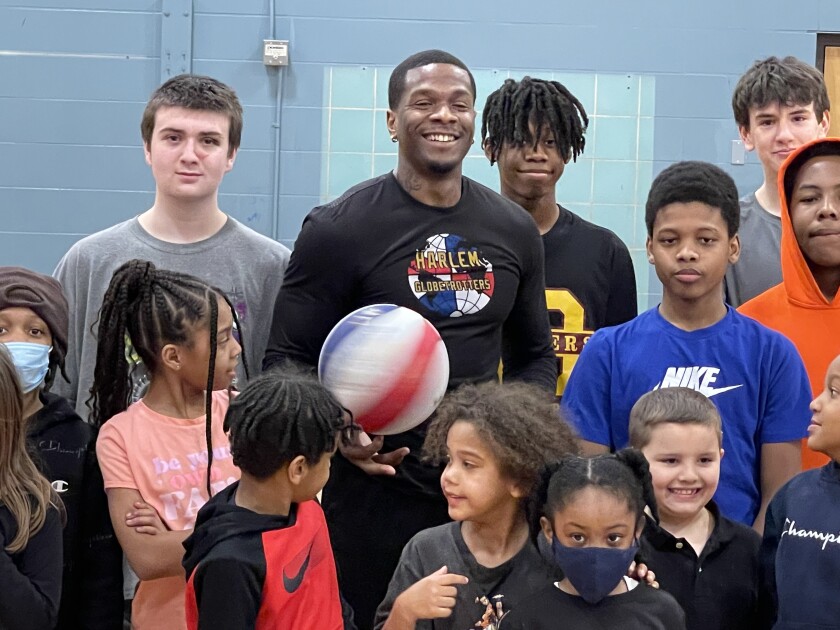 Harlem Globetrotter Flip White stands smiling, holding basketball, amid crowd of children posing for group photo.