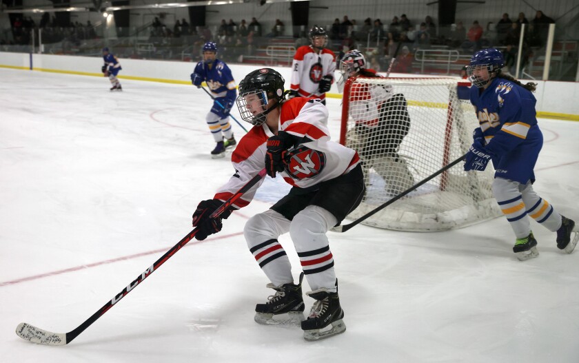 Trojans Cadence Van Ede passes the puck out from behind the Worthington goal pursued by Windom Eagles Marissa Becker during a Thursday evening game.