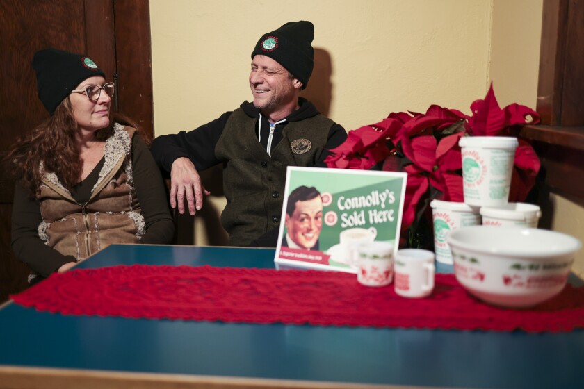 Red, white and green holiday Tom and Jerry beverage items, female in glasses, male in winter hat