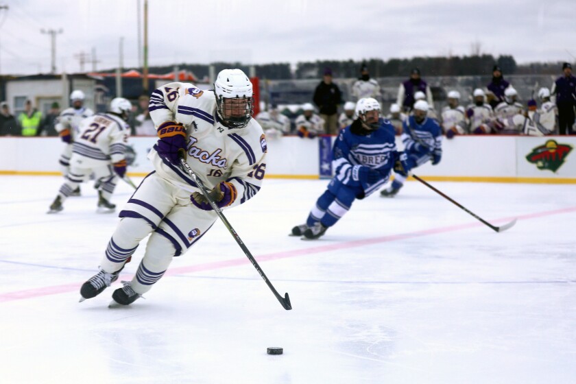 A high school boys hockey player controlling the puck during an outdoor game.