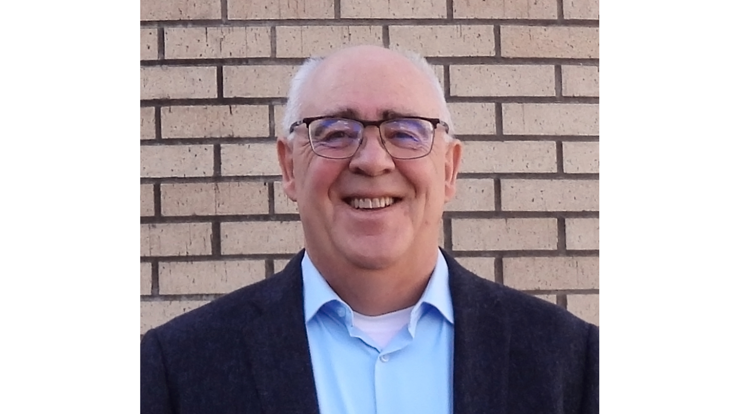 Headshot of a man standing in front of a brick wall.