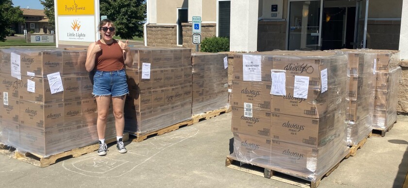 A woman gives a thumbs up in front of dozens of heavily wrapped parcels on pallets, marked Always.