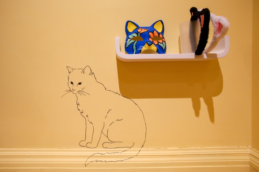 One of the activities at The Rourke's show, Gallery Cats, is spotting the seven cat drawings hidden on the walls in the Children's Gallery. An outline drawing of a cat on a yellow wall. Next to it is a shelf on wall with two cat masks on it.