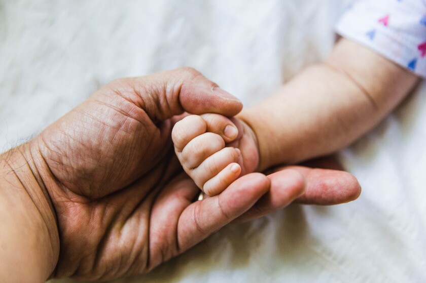 A baby's hand is cradled in a father's hand.