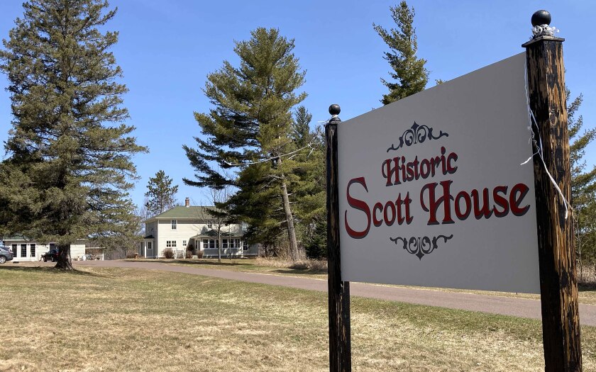 A sign at the end of a driveway with a house in the background